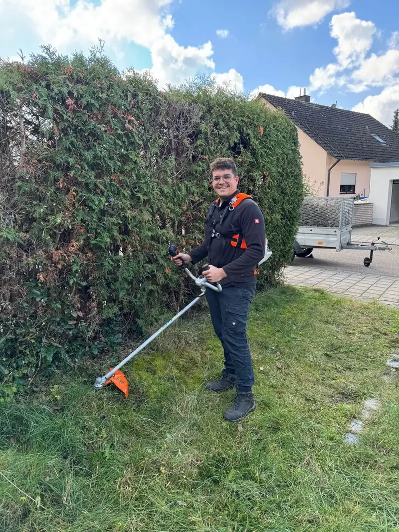 Moritz mit dem Freischneider vor einer Thujahecke
